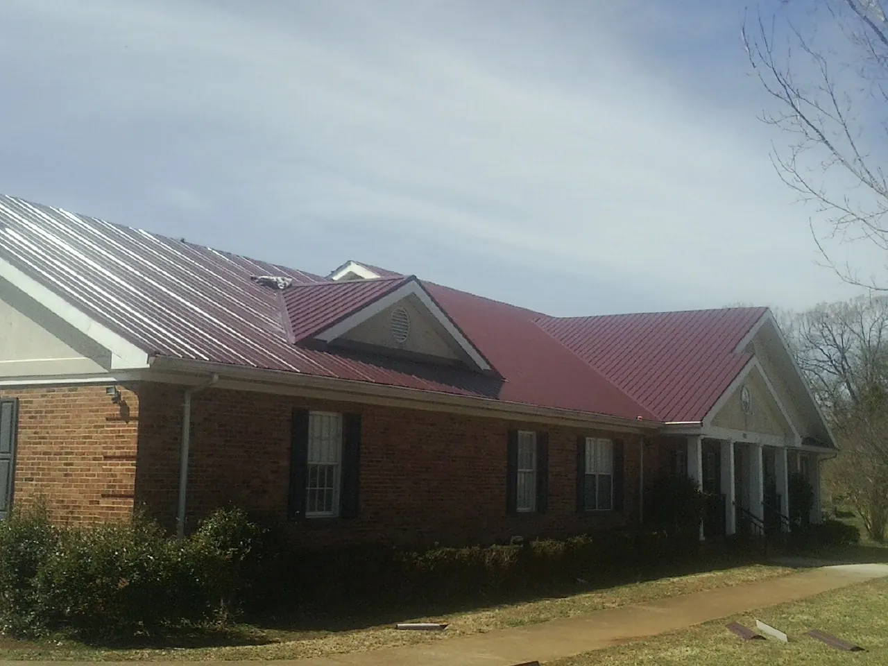 Red metal roof with gabled entries on a long brick building, from a Hail Damage Roof Repair job in Rainbow City
