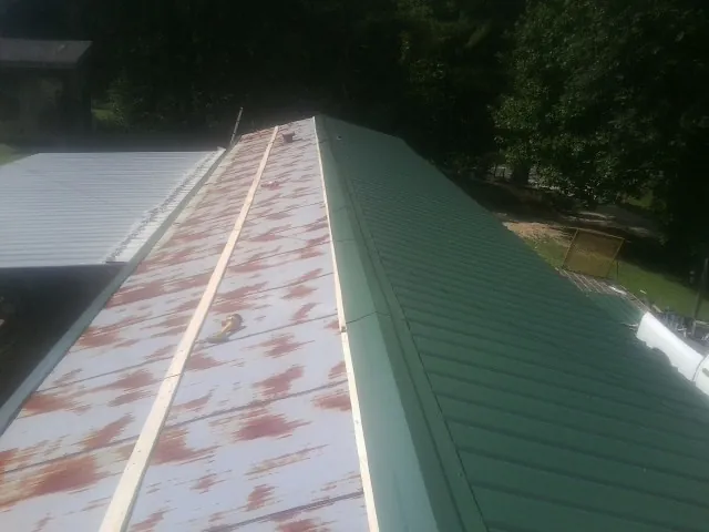 Old rusted panels beside newly installed green metal roofing — Wind Damage Roof Repair by Roofing Brothers in Rainbow City