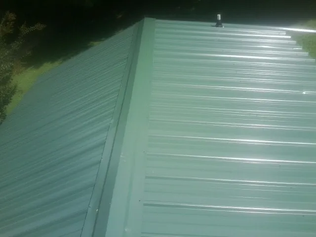 New green metal panels meeting at the ridge of a roof — Flat Roof Repair work by our crew in Rainbow City