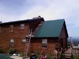 Green metal roof going on a two story log home with ladders set in Rainbow City