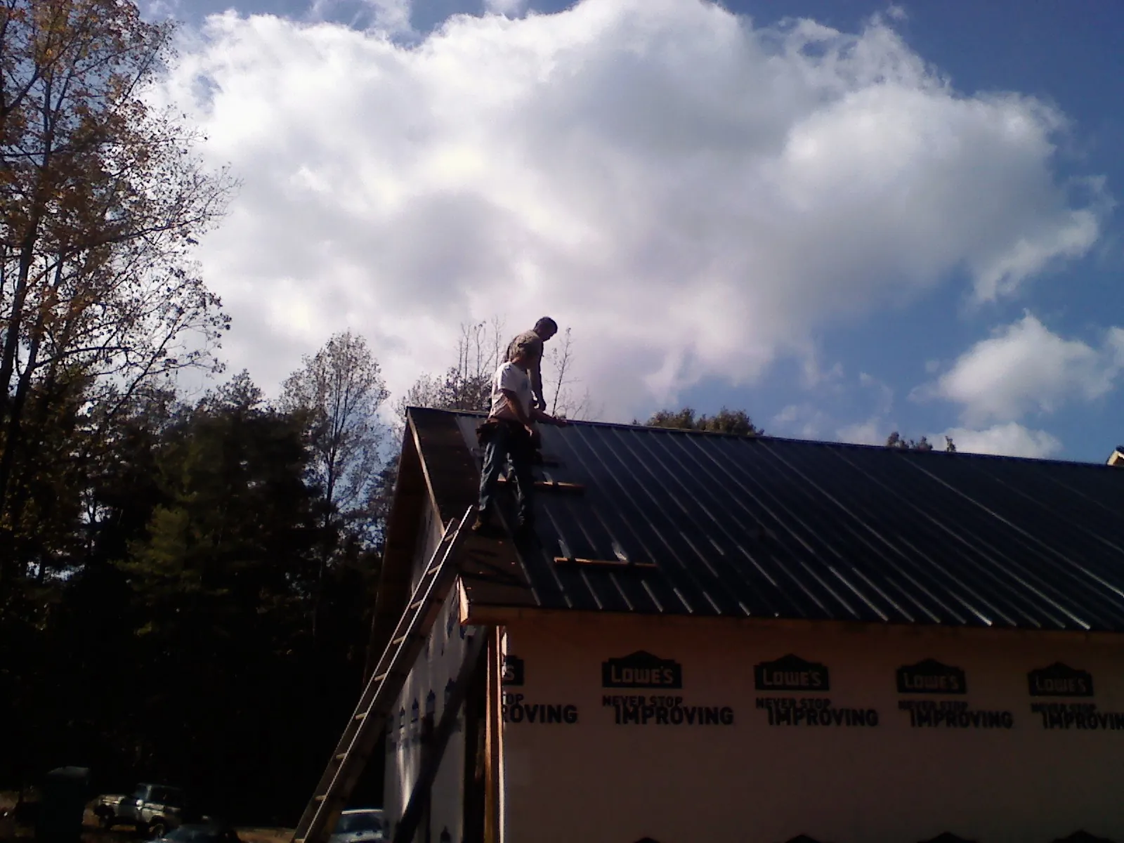 Roofer fastening dark metal panels high against a cloudy sky, from a Roof Inspection job in Rainbow City