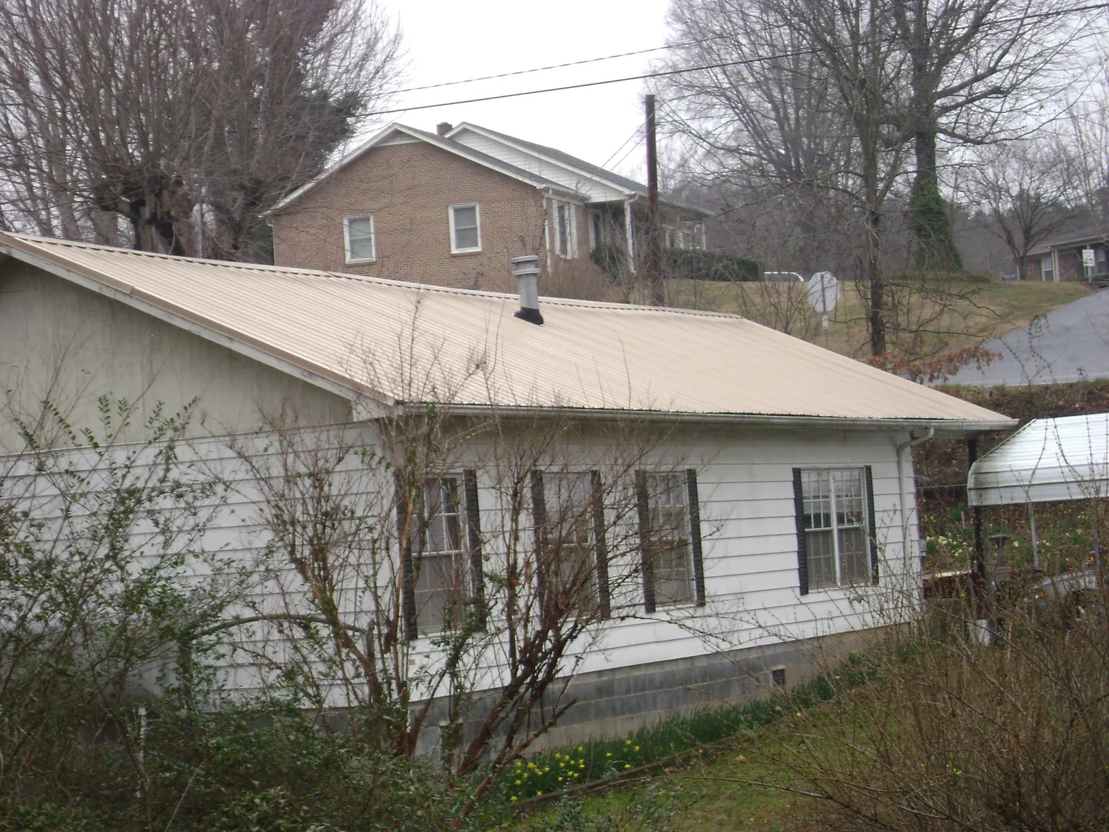 Tan metal roof on a white sided house set into a hillside — Commercial Roofing by Roofing Brothers in Rainbow City