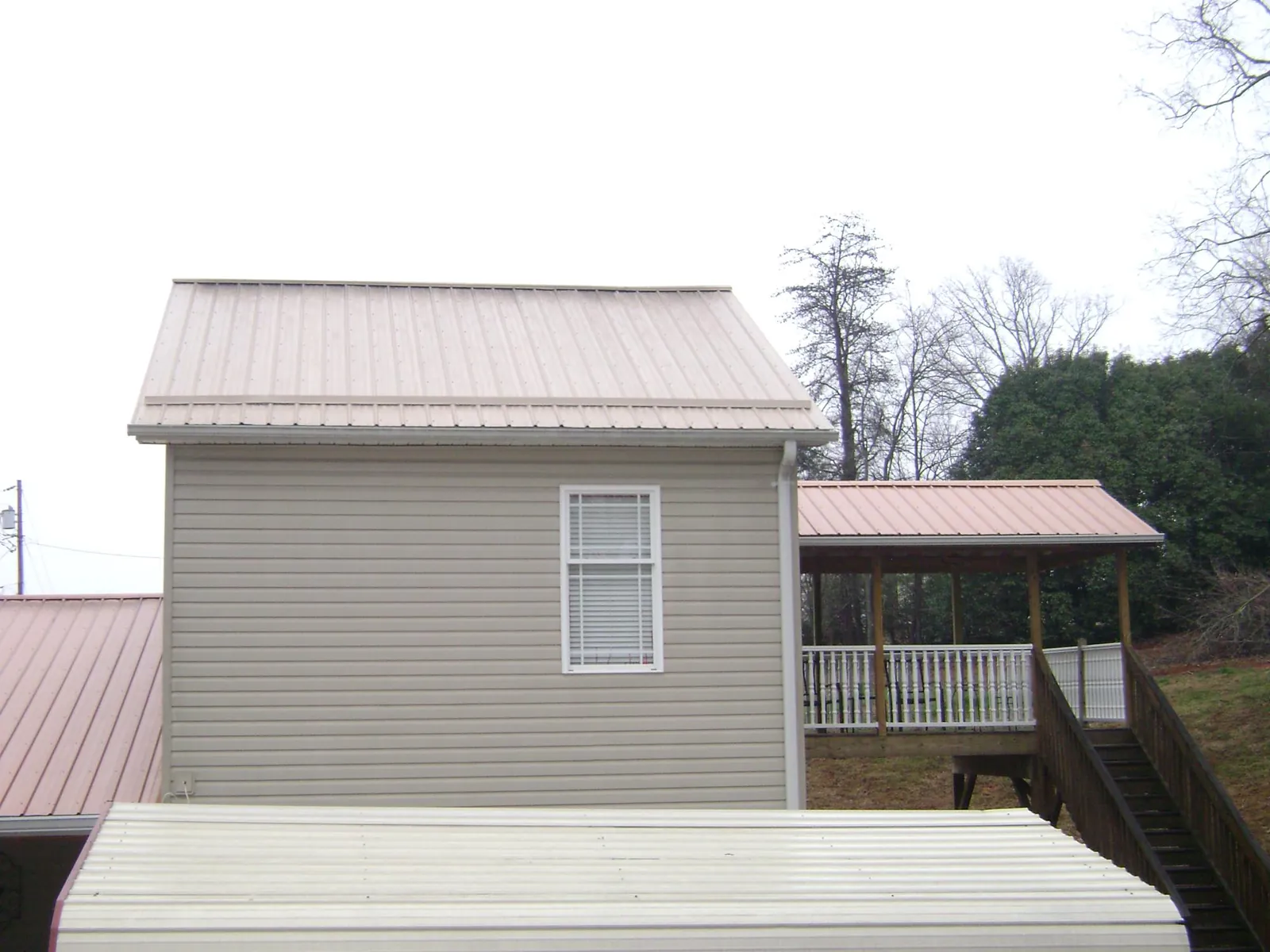 Tan metal roofs on a two story addition and attached porch, from a Roof Replacement job in Rainbow City